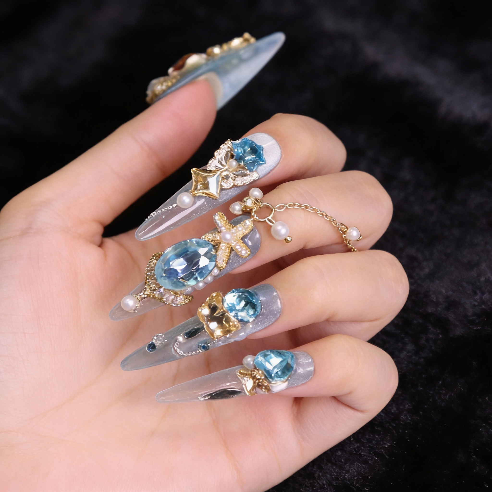 Close-up of ocean blue luxury press on nails with pale amber crystals, pearl details, and orange-red shell zircon centerpiece