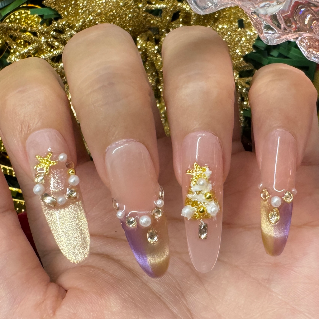 Hand wearing gold and purple gradient Christmas press on nails decorated with pearls, stars and festive holiday accents.