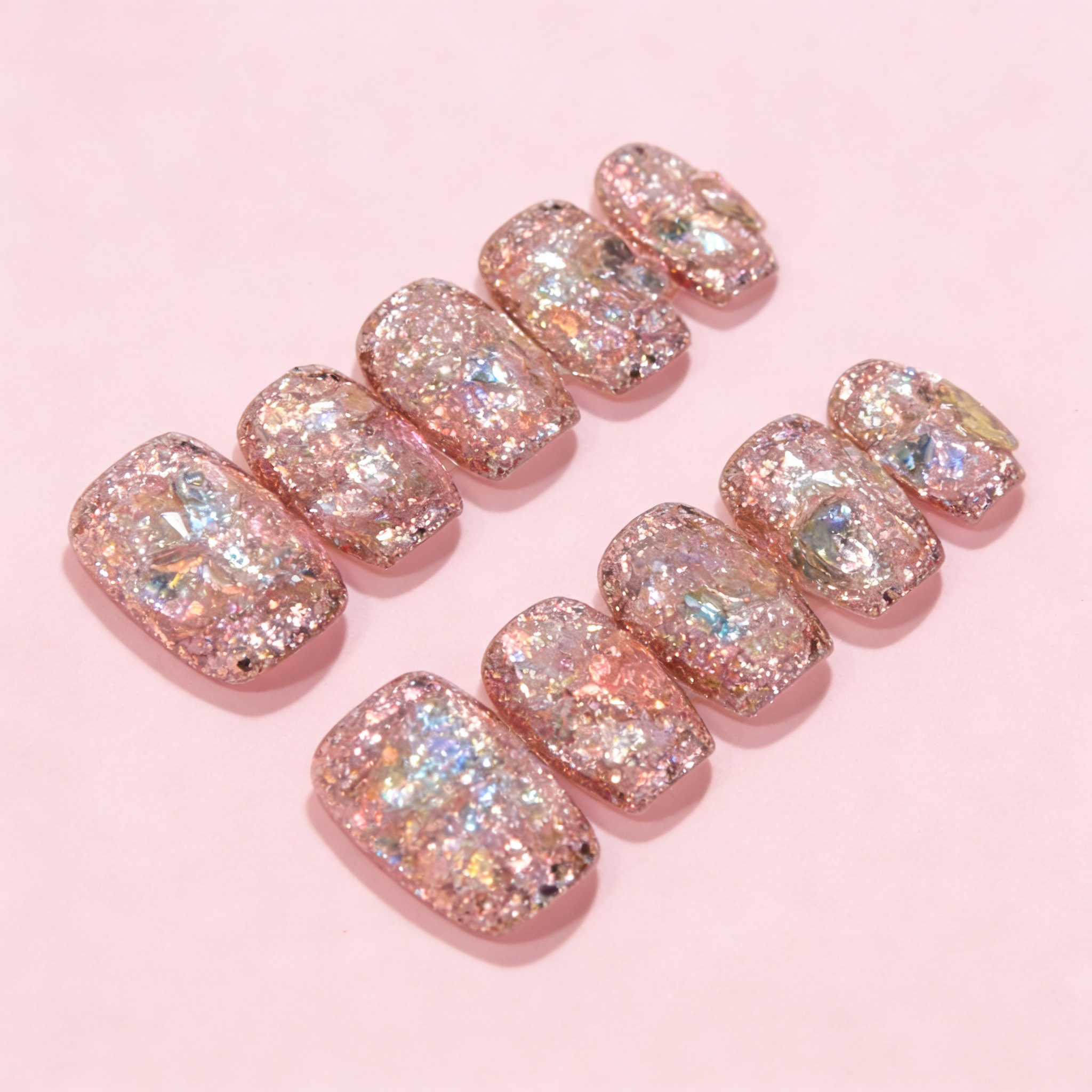 Pink winter sparkly press on nails with translucent base and iridescent aurora shimmer, minimal glitter design on a soft pink background.