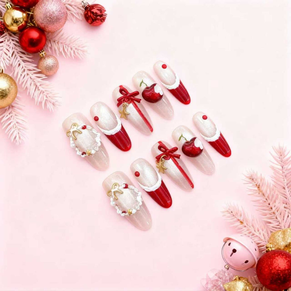 Red and nude Christmas press on nails with 3D cherry ornaments, gold bows, white trim details and festive gift-inspired accents arranged on a pink background.