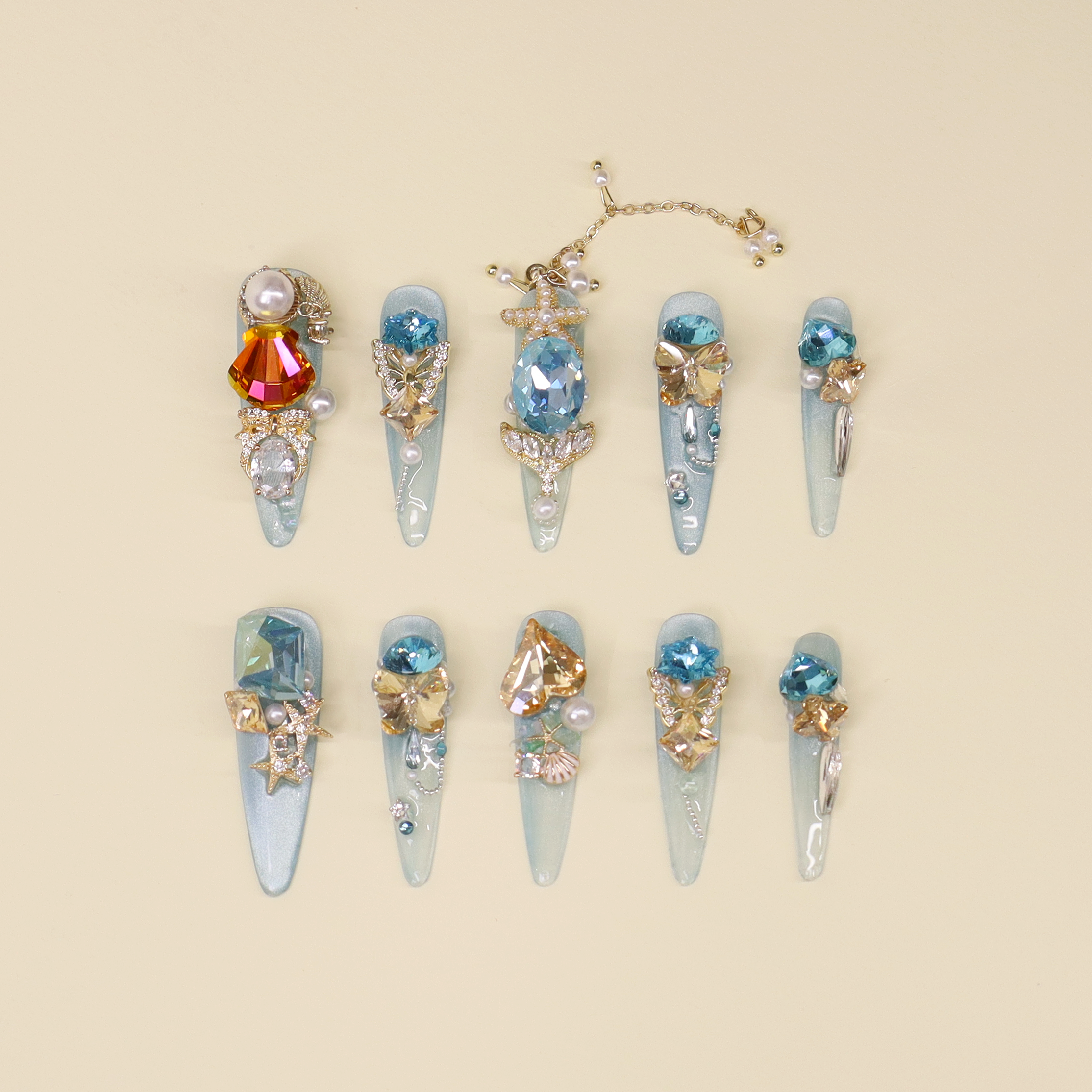 Luxury ocean blue press on nails featuring sea-blue and amber crystals, pearl accents, mermaid tail details, and a vivid orange-red shell zircon inspired by Mera, Queen of Atlantis