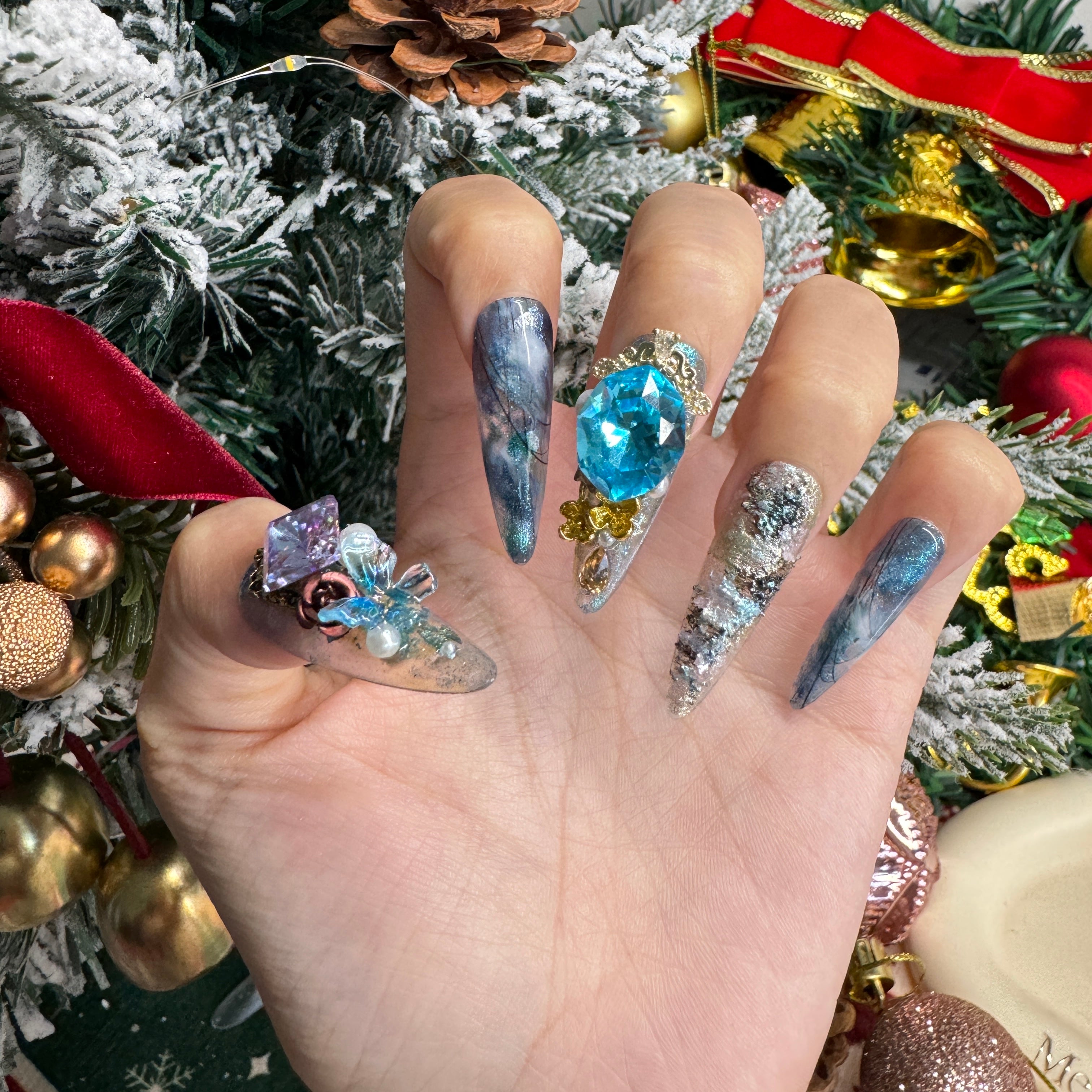Luxury blue Christmas press on nails with a large sapphire gemstone, glacier marbling, silver foil textures and handcrafted floral crystal details.