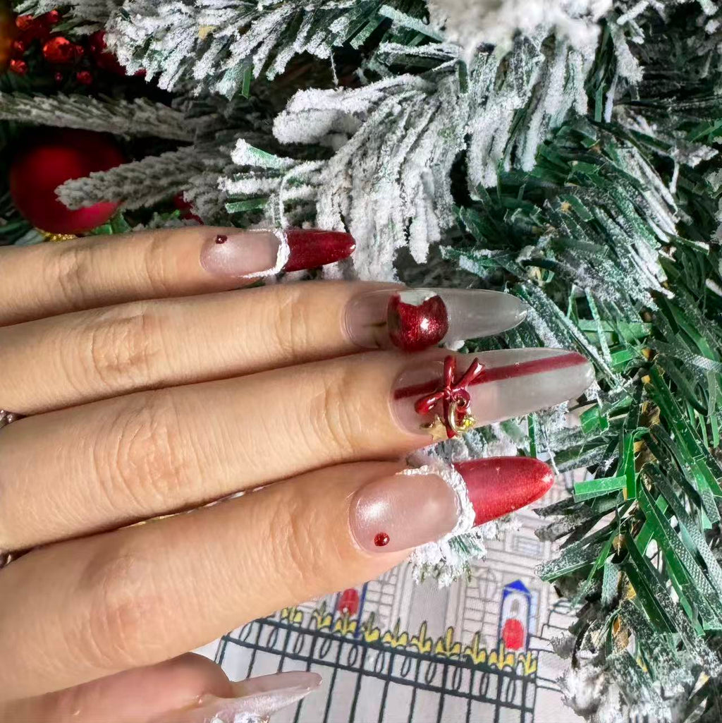 Hand holding Christmas decor while wearing red gift-inspired nails decorated with cherry ornaments, white trim and gold bow details.