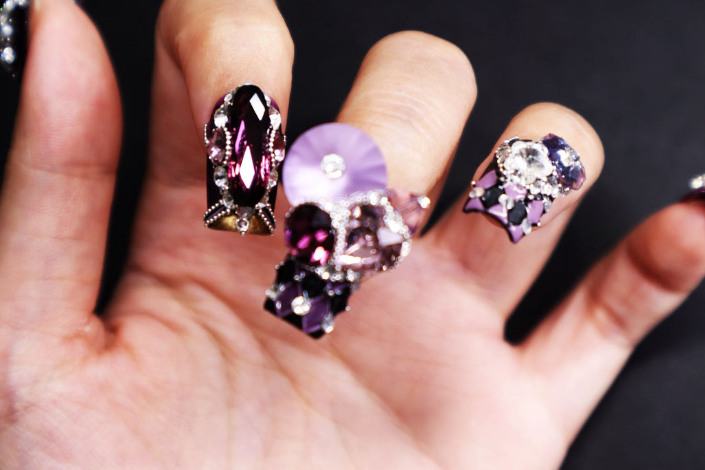Close-up of luxury short nails with deep violet tones, Swarovski crystals, and high-jewelry inspired detailing.