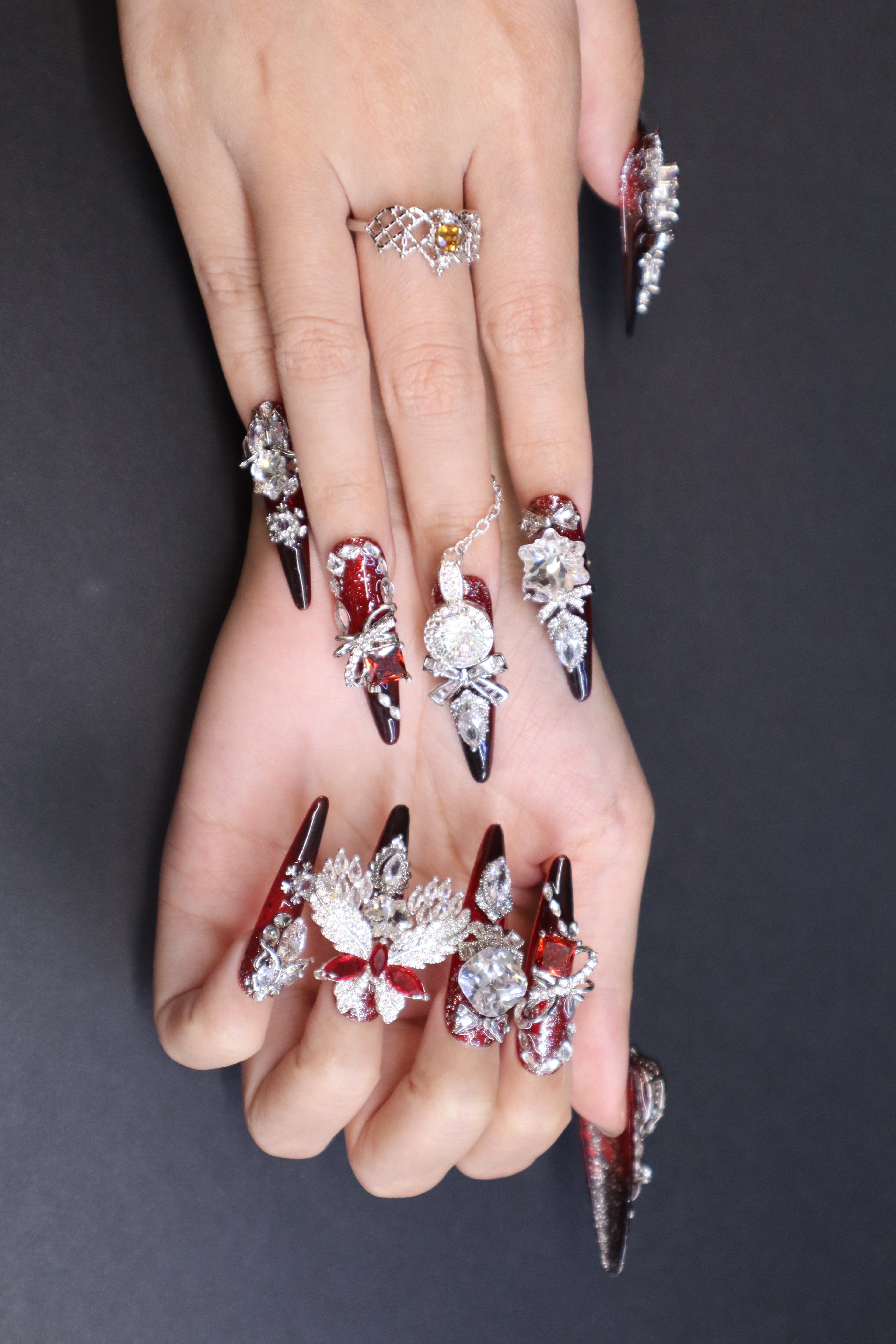 Crimson Seraph luxury press-on nails with red and black gradient, blood-red crystal, silver wing detail, and statement nail ring