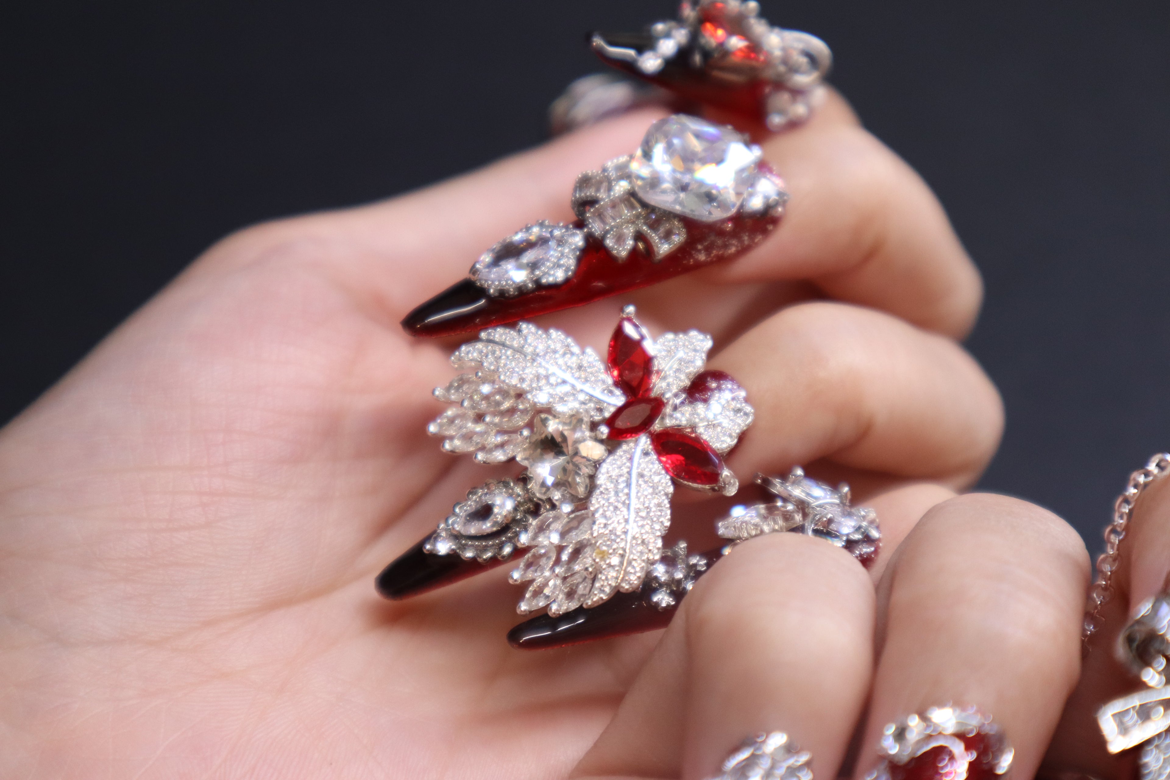 Luxury crystal press-on nails with blood-red gemstone, silver wing design, and disco crystal detail