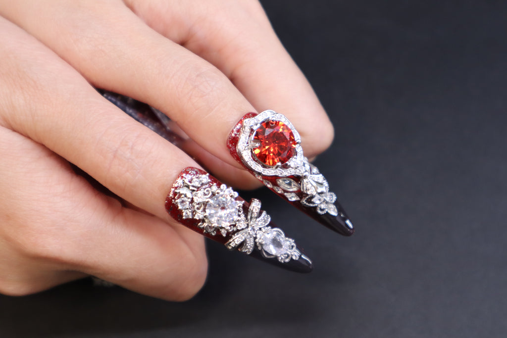 Luxury crystal press-on nails with blood-red gemstone, silver wing design, and disco crystal detail