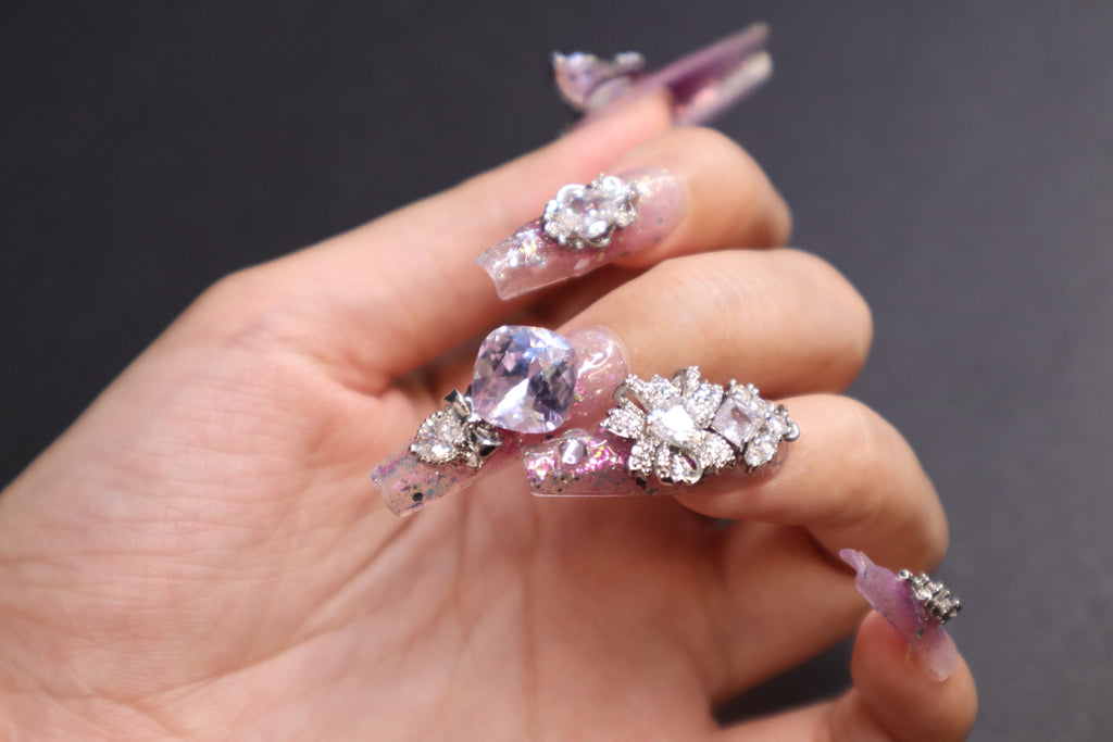 Lilac Heartbeat purple press-on nails with sheer glitter base, lilac blush gradient, butterfly crystal accents, and movable heart charm design.