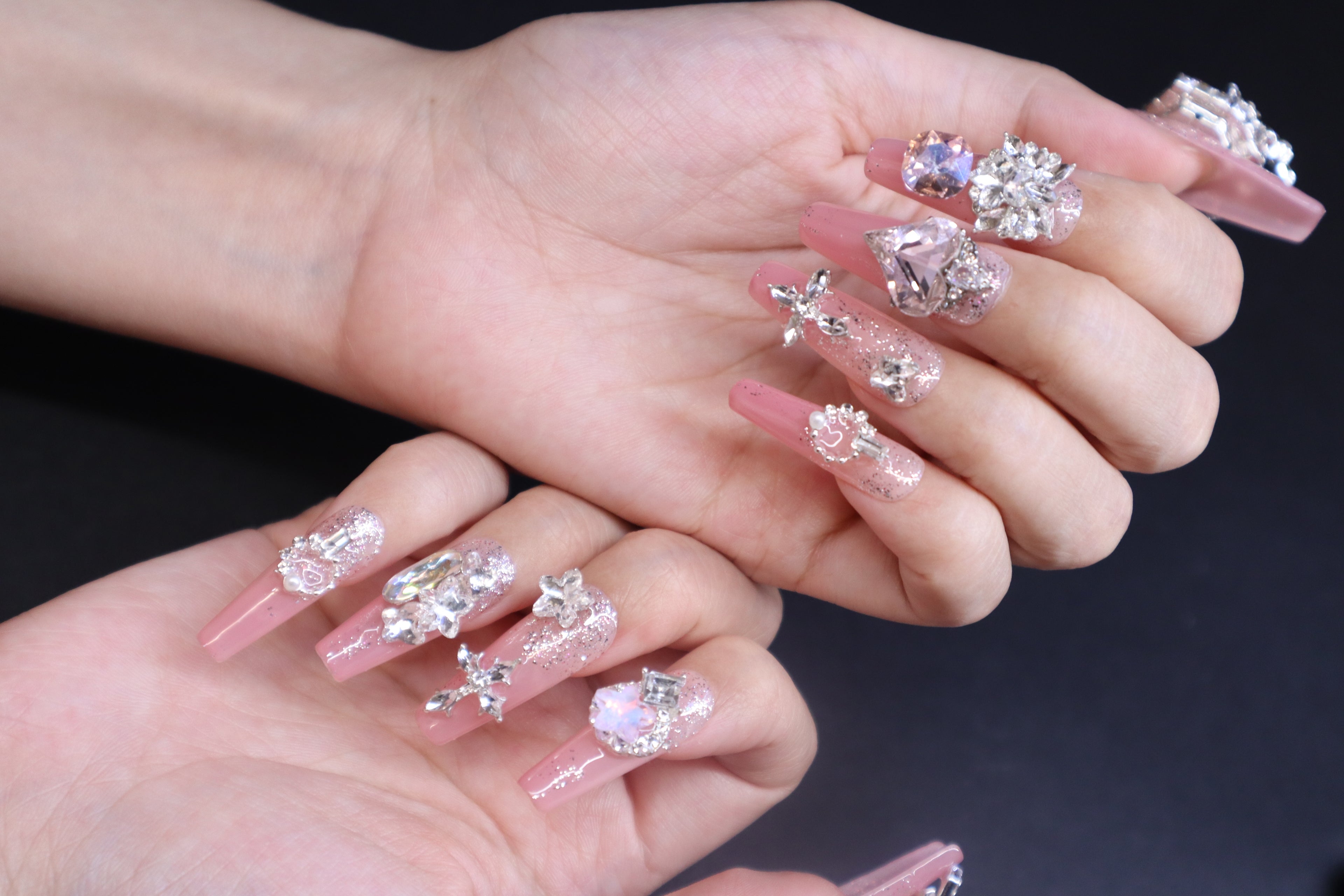 Sweet pink crystal press-on nails with heart-shaped gem and soft feminine finish on hands