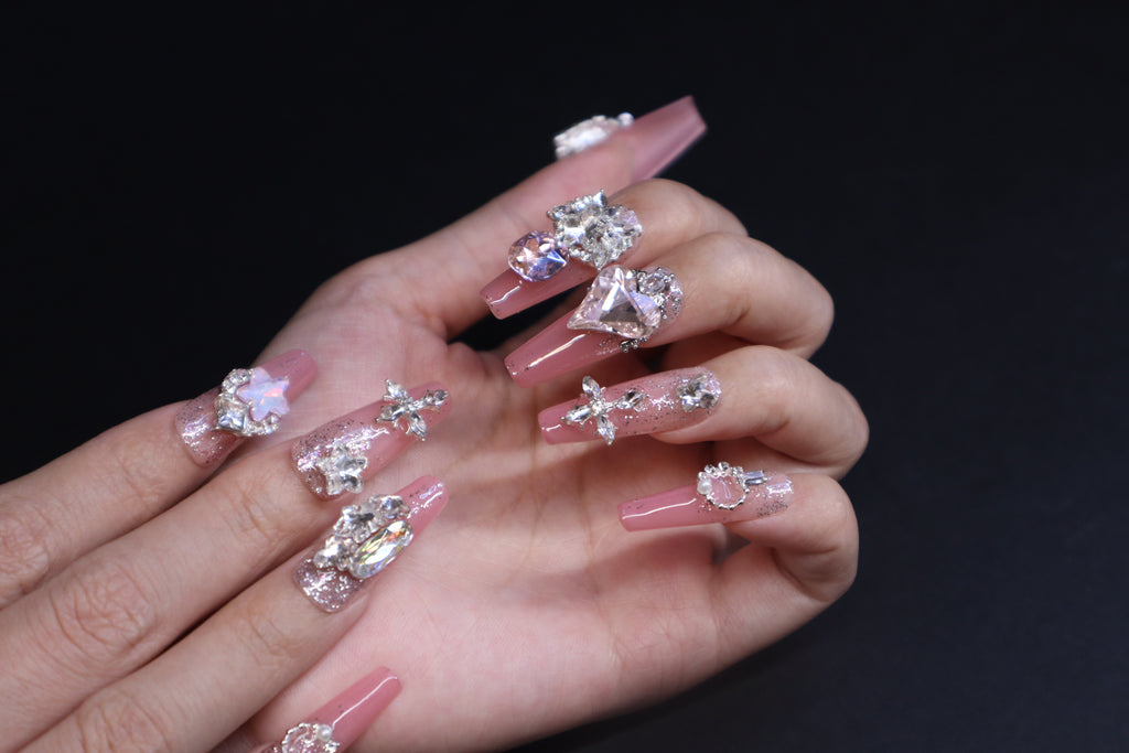 Sweet pink crystal press-on nails with heart-shaped gem and soft feminine finish on hands