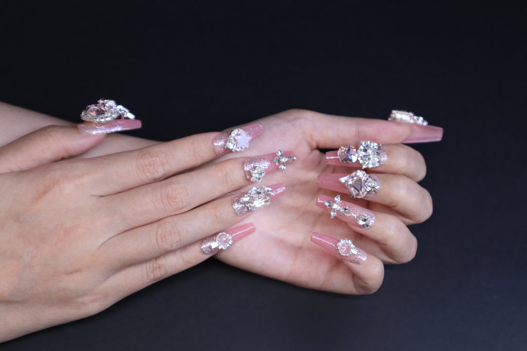 Soft baby pink glitter gradient press-on nails with heart crystal and marquise accents worn on hands