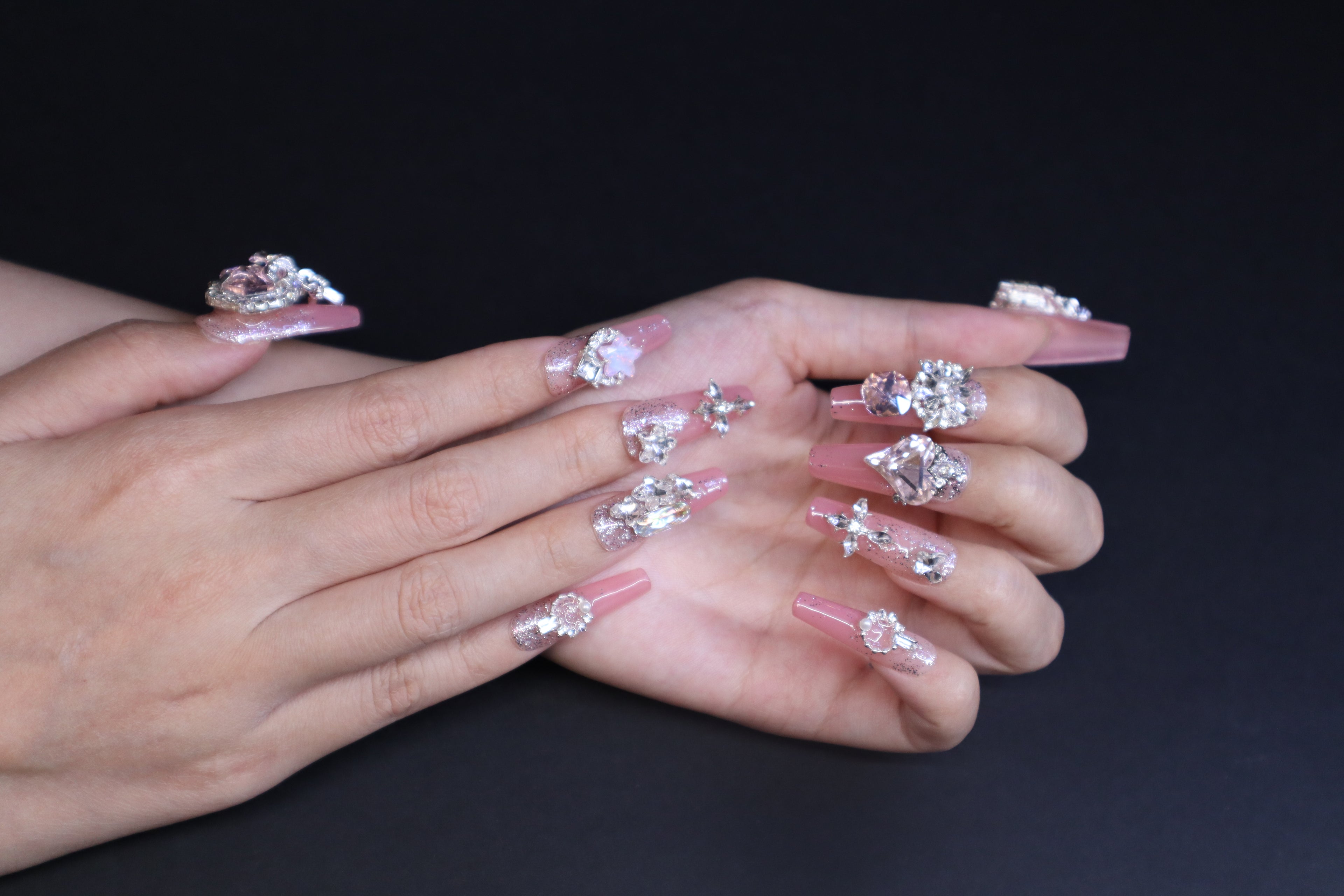 Soft baby pink glitter gradient press-on nails with heart crystal and marquise accents worn on hands