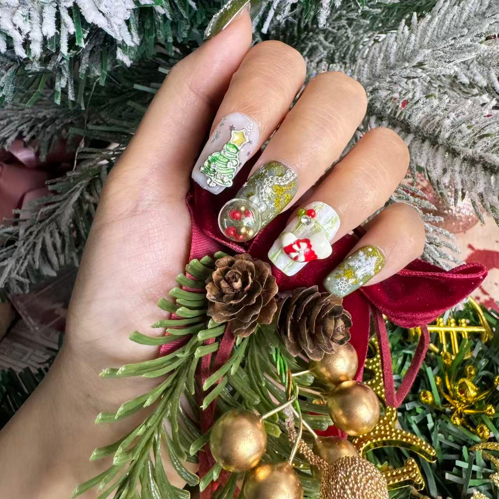 Festive green Christmas nails with 3D charms, snowflake art and cat-eye shimmer, photographed with snowy holiday decorations.