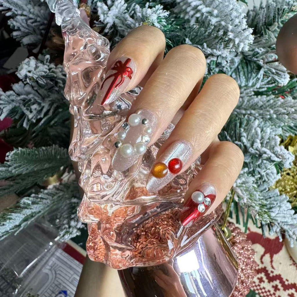 Close-up of red and pink Christmas press on nails featuring pearls, metallic accents and ribbon details, photographed with a pink crystal Christmas tree.