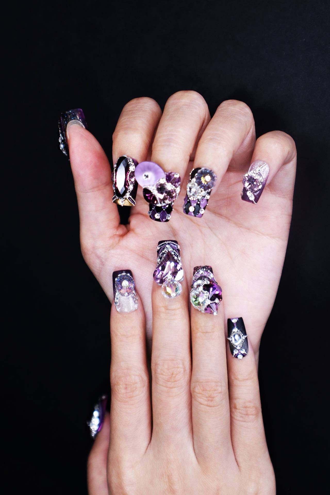 Short luxury violet press-on nails worn on hand with sculptural crystal embellishments and refined oriental-inspired nail art.