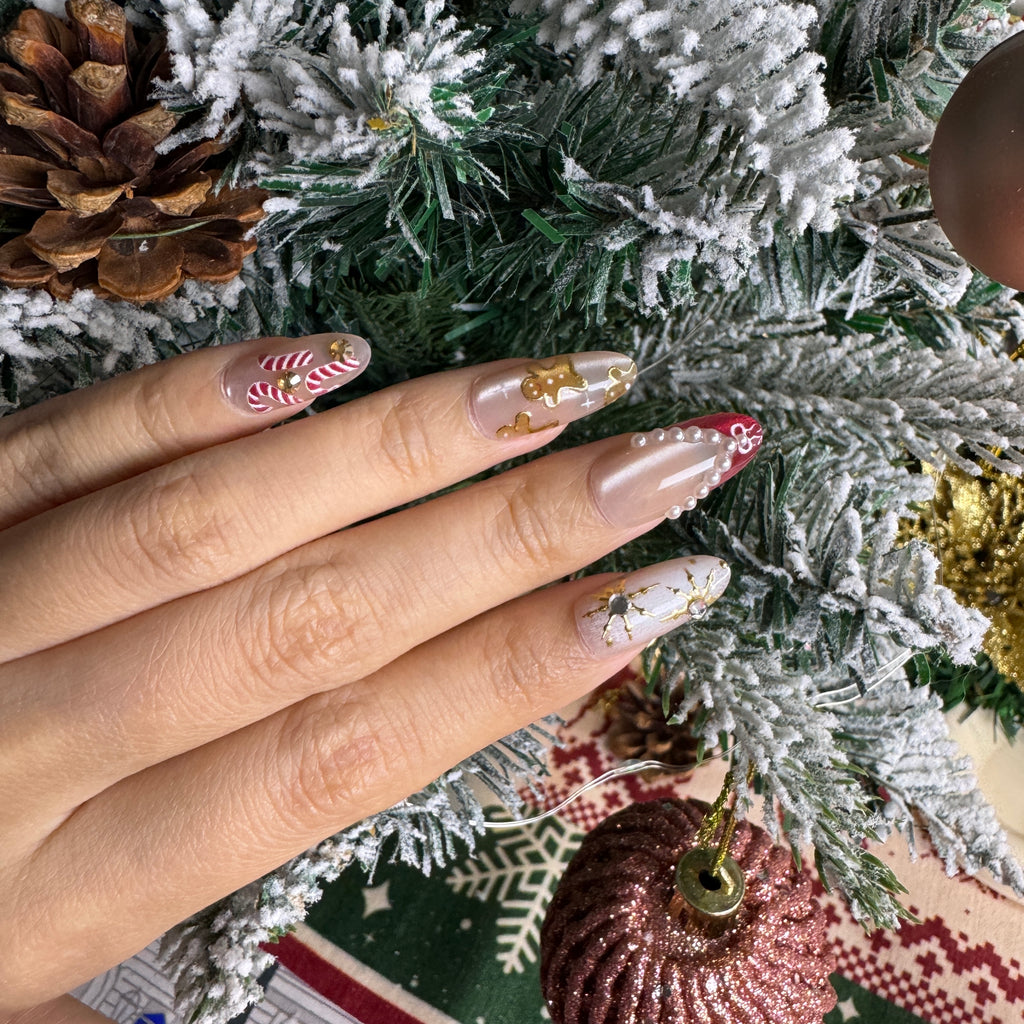 Cute Christmas nails with gingerbread art, candy canes and gold accents, photographed against snowy pine branches.